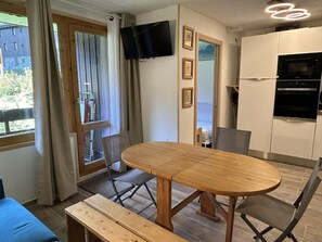 A modern kitchen with a built-in oven, a dining table with chairs, and a TV mounted on the wall. - 110m from shops, view building, balcony, tv, 25m², Méribel-Mottaret (Méribel - Les Allues)