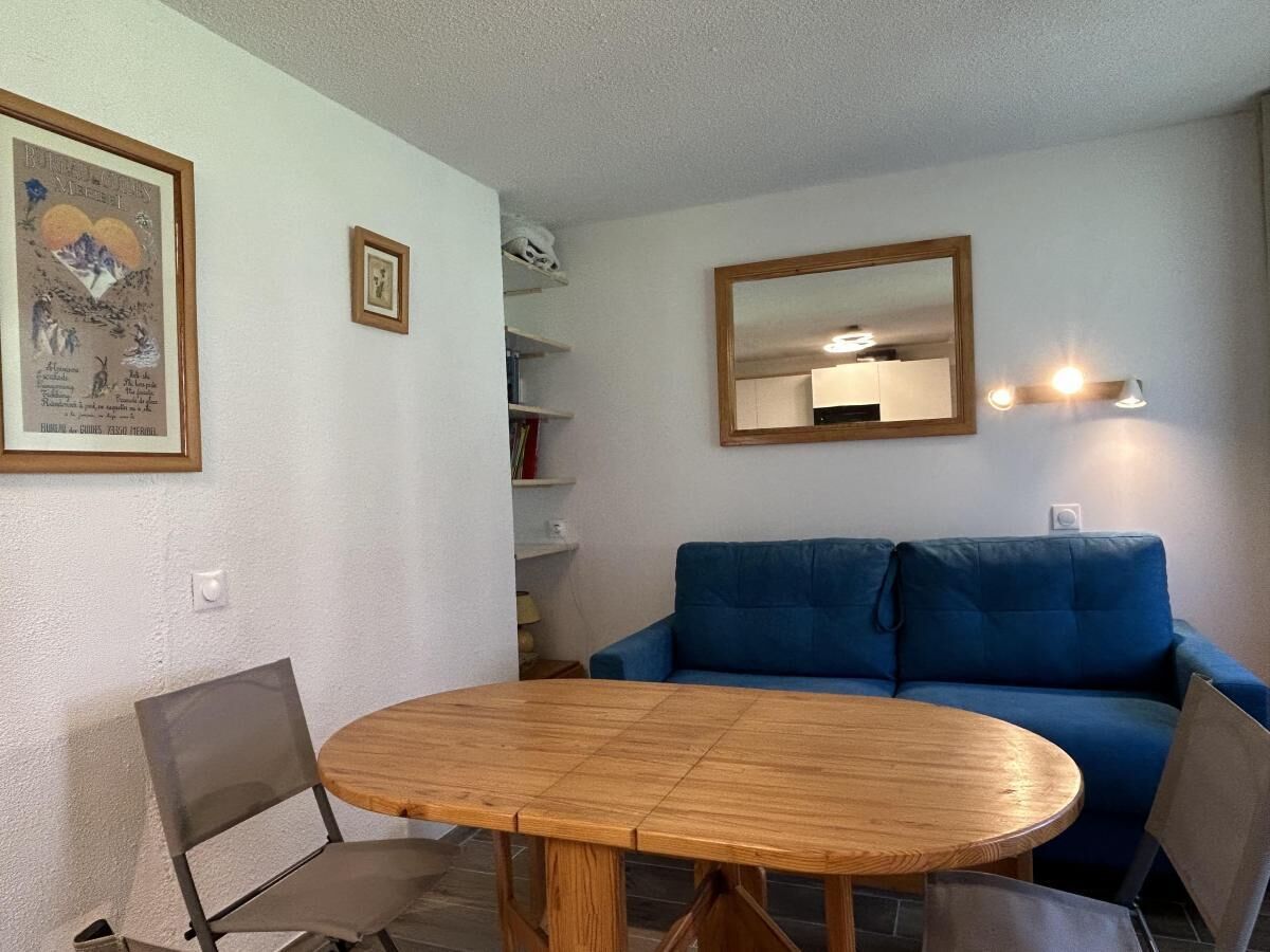 A room with a wooden dining table, two chairs, a blue sofa, a wall-mounted mirror, and framed pictures.