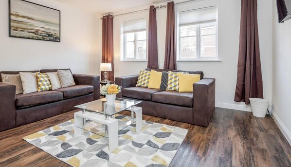 A living room with two brown sofas, a glass coffee table, and a patterned rug.
