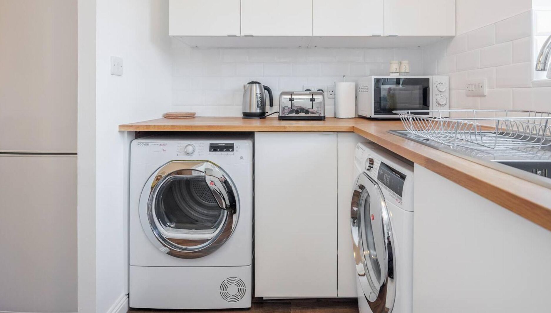 A compact kitchen with a washing machine, a dishwasher, a microwave, and a toaster.