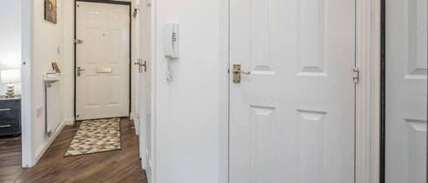 A hallway with a patterned rug, a white door, and a thermostat on the wall.