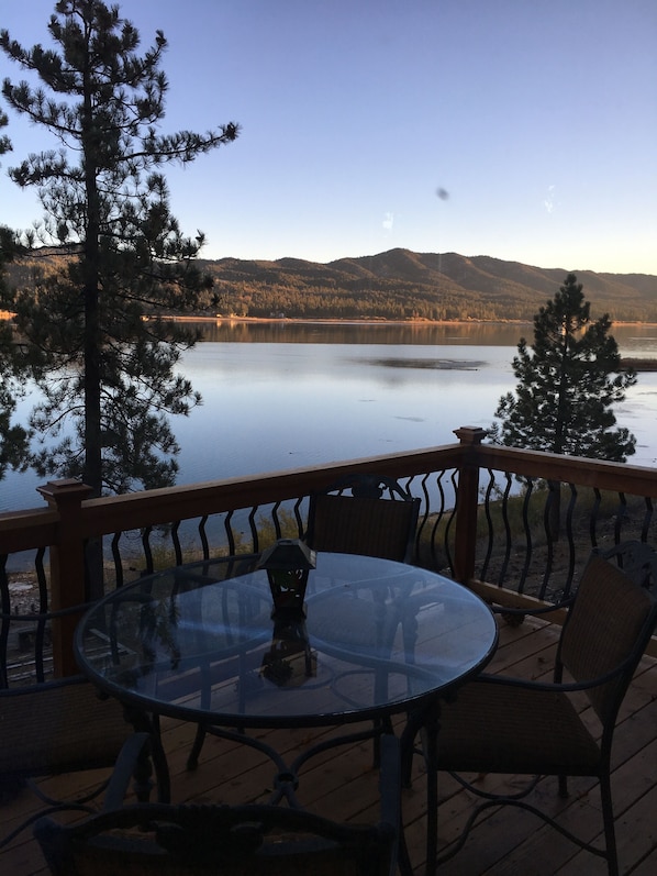 Una terraza con mesa y sillas de vidrio que da a un lago tranquilo y colinas boscosas.