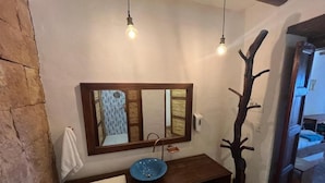 A bathroom with a wooden vanity, a blue basin, a large mirror, and pendant lights.