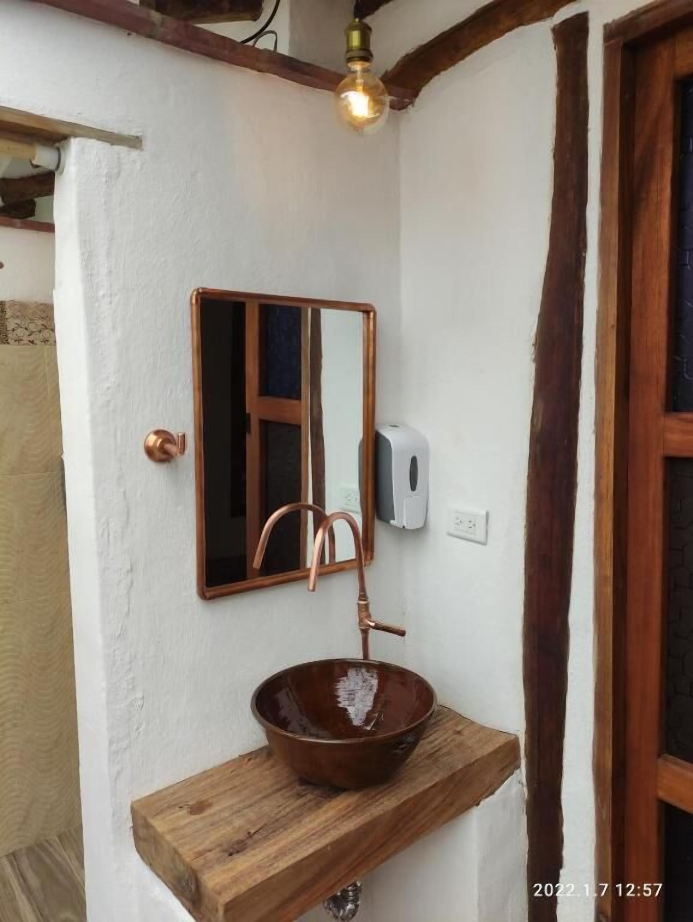 A bathroom with a wooden shelf holding a copper sink, a mirror, and a hand soap dispenser.