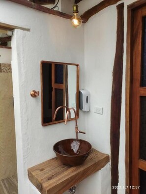 Casa de banho com uma estante de madeira que suporta uma pia de cobre, um espelho e um dispensador de sabonete líquido.