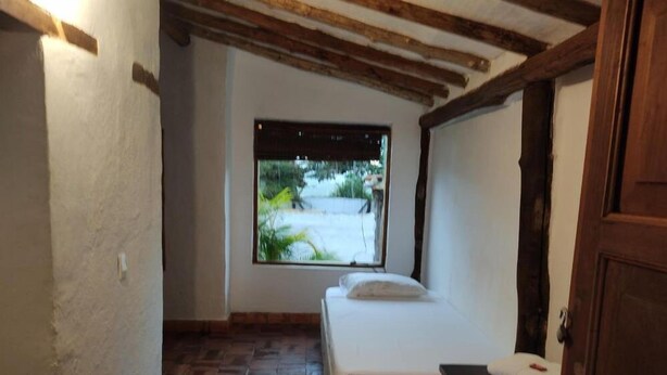 Una habitación pequeña y acogedora con una cama individual, una ventana con vistas a la vegetación y un techo de madera.