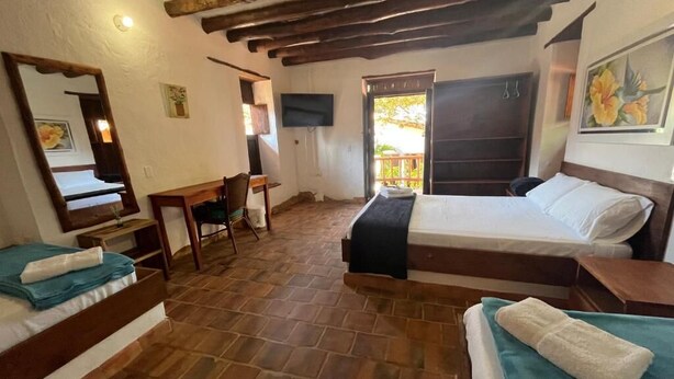 A room with two beds, a desk, a chair, a TV, and a door leading to an outdoor area.