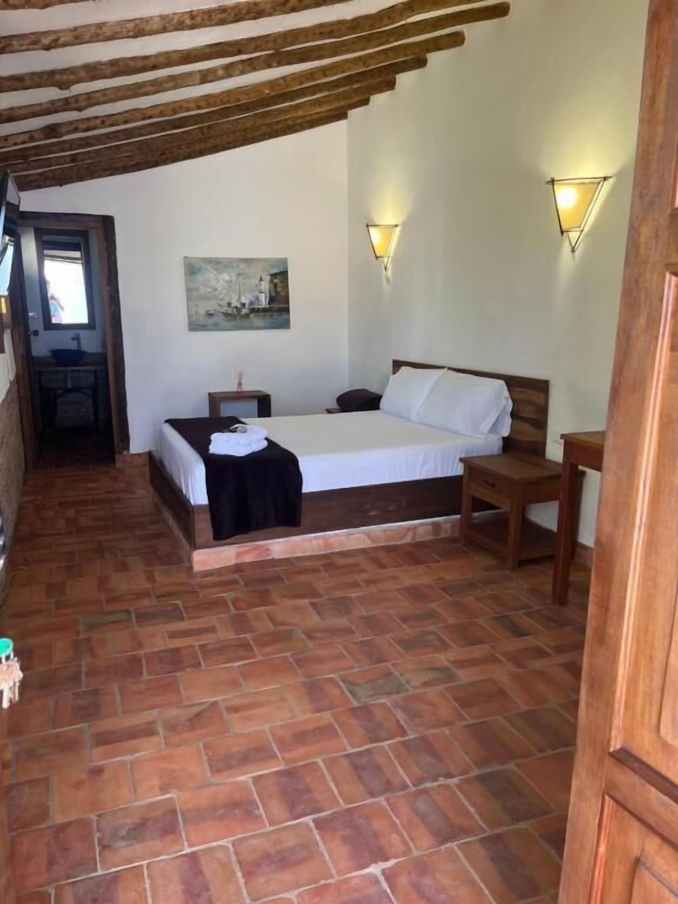 A bedroom with a wooden bed, a nightstand, a small table, and a painting on the wall.