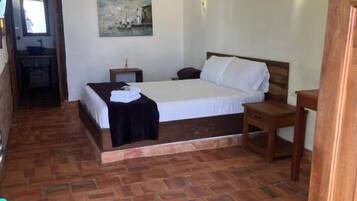 A bedroom with a wooden bed, a nightstand, a small table, and a painting on the wall.
