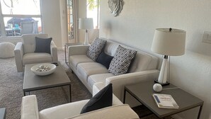 A modern living room with a sofa, armchairs, and a coffee table. There are decorative wall pieces and a lamp on a side table. - Lake House Pool & Palms (Goodyear)
