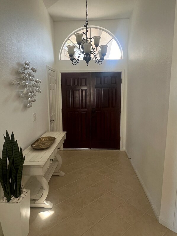 A hallway with a dark wooden door, a white bench, a potted plant, and a chandelier.
