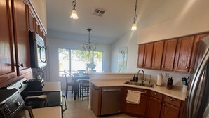 A modern kitchen with wooden cabinets, stainless steel appliances, and pendant lighting. - Lake House Pool & Palms (Goodyear)