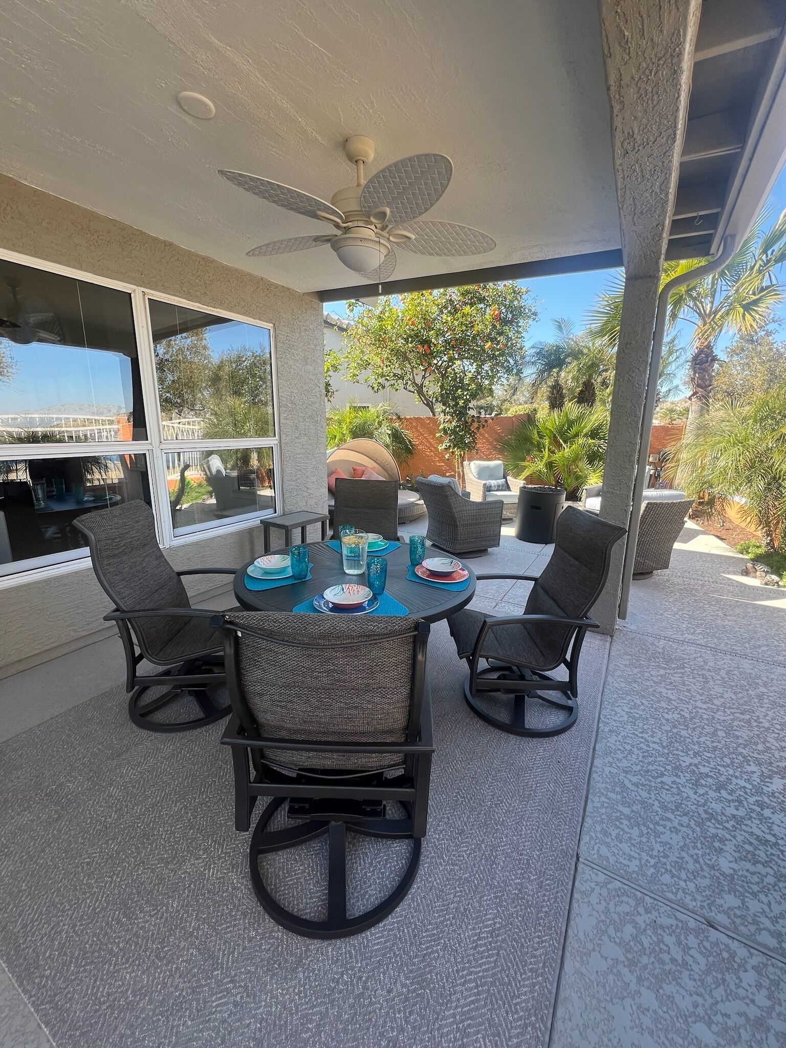 Une terrasse extérieure avec une table ronde, quatre chaises et un ventilateur de plafond.
