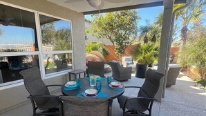 An outdoor patio with a round table, four chairs, and a ceiling fan. - Lake House Pool & Palms (Goodyear)