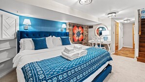 A modern hotel room with a large bed, a blue accent wall, a decorative flower painting, and a small desk with a chair. - The Cavalier - Quiet Corner of Old Town (Alexandria)