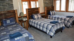 A room with three beds, each with a plaid bedspread and pillows, wooden headboards, and a stone wall.