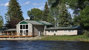 A lakeside cabin with a stone exterior, large windows, and a wooden deck.