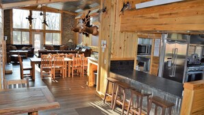 A rustic cabin interior with a dining area, kitchen, and a living room with a fireplace.