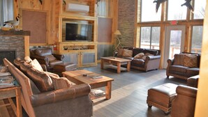 A cozy lodge interior with leather sofas, a fireplace, a TV, and wooden walls.
