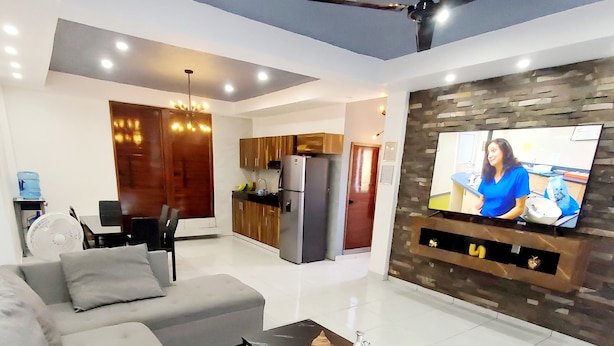 Uma sala de estar moderna com um sofá cinzento, uma mesa de centro e uma televisão de tela plana na parede.