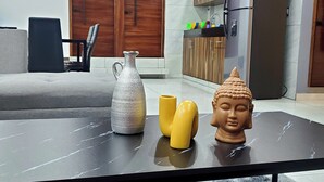 Uma sala de estar moderna com uma mesa de centro preta, uma escultura de cabeça de Buda e um vaso.