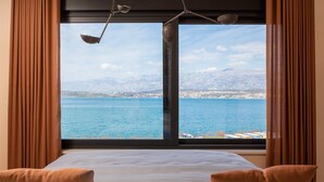 Un dormitorio con un gran ventanal que da a una masa de agua y montañas lejanas.