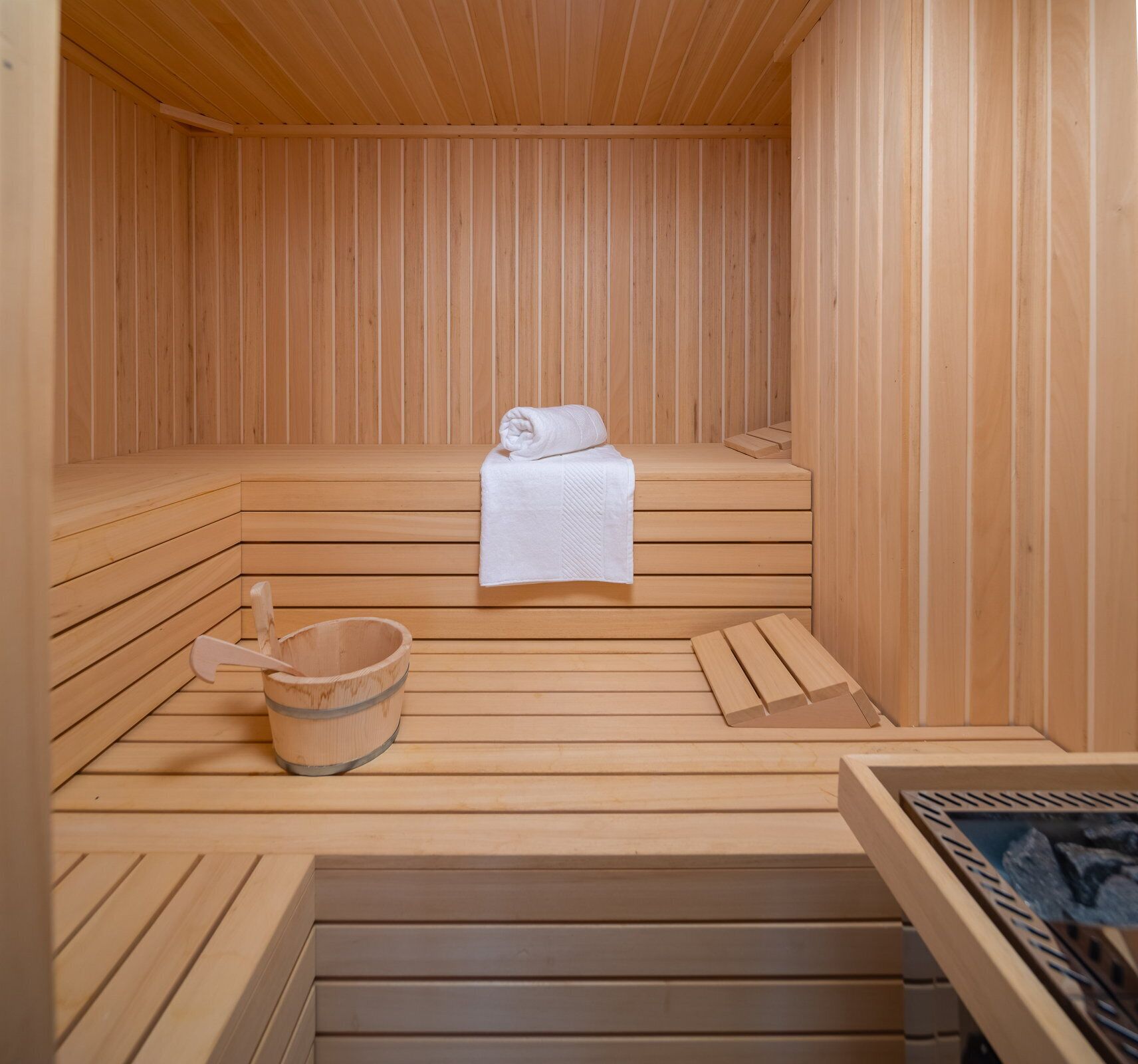 Uma sauna de madeira com bancos, uma toalha e um balde de madeira.