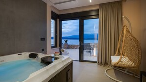 Un baño moderno con bañera, cabina de ducha de vidrio y vistas a un lago y montañas a través de amplios ventanales.
