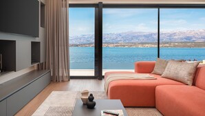 Una sala de estar moderna con un ventanal que ofrece vistas a un lago y montañas.