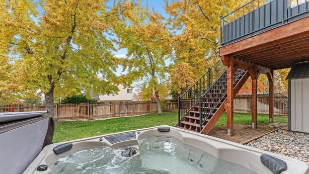 Un bain à remous dans un jardin, avec une terrasse en bois et des escaliers menant à une zone abritée.