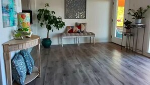 A modern living room with a wooden floor, a bench, a potted plant, and a decorative wall piece. - Beautiful lakefront home new to market (Hot Springs)