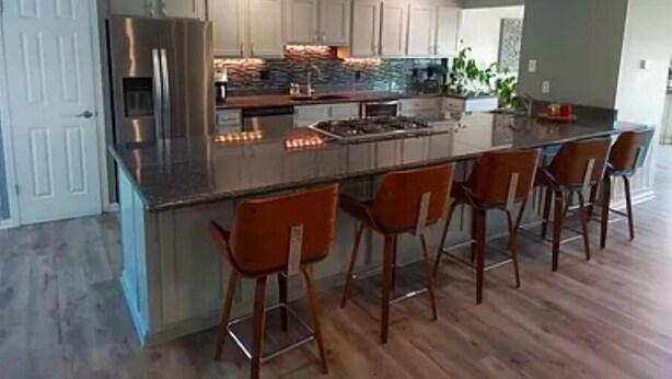 A modern kitchen with a large island, bar stools, and a stainless steel refrigerator. - Beautiful lakefront home new to market (Hot Springs)