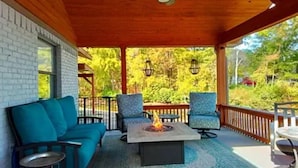 A covered outdoor seating area with a fire pit, chairs, and a view of the surrounding greenery. - Beautiful lakefront home new to market (Hot Springs)