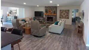 A spacious living room with a fireplace, a television, and a dining area with a table and chairs. - Beautiful lakefront home new to market (Hot Springs)