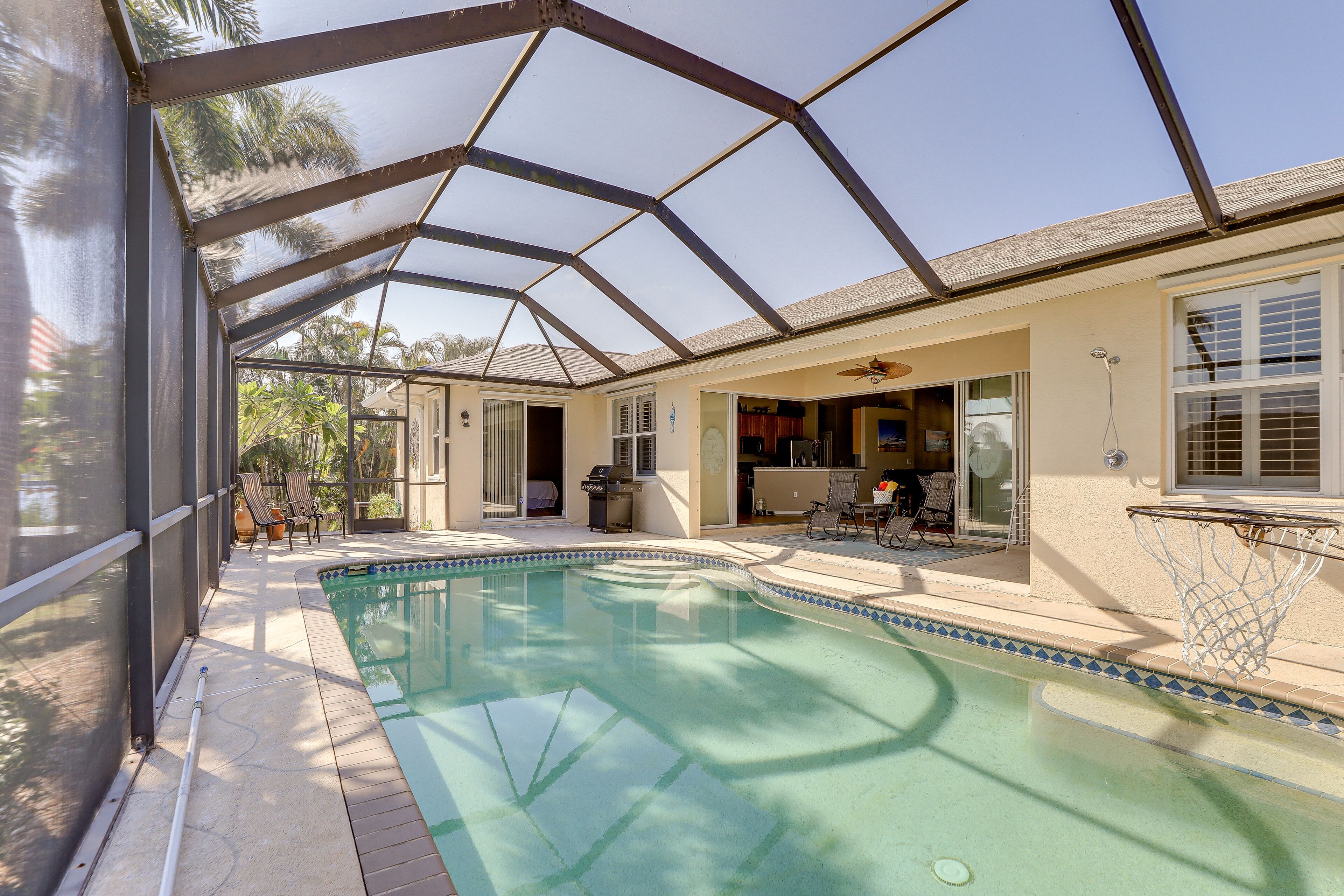 Ein überdachter Pool mit Metallveranda, neben einem Haus mit Terrasse und Gartenmöbeln.