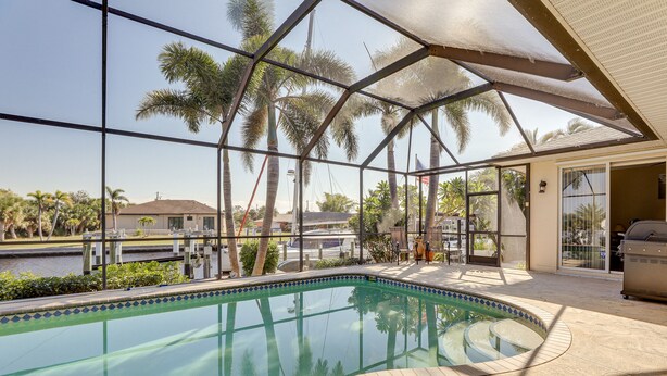 A swimming pool with a glass enclosure, palm trees, and a view of a body of water.