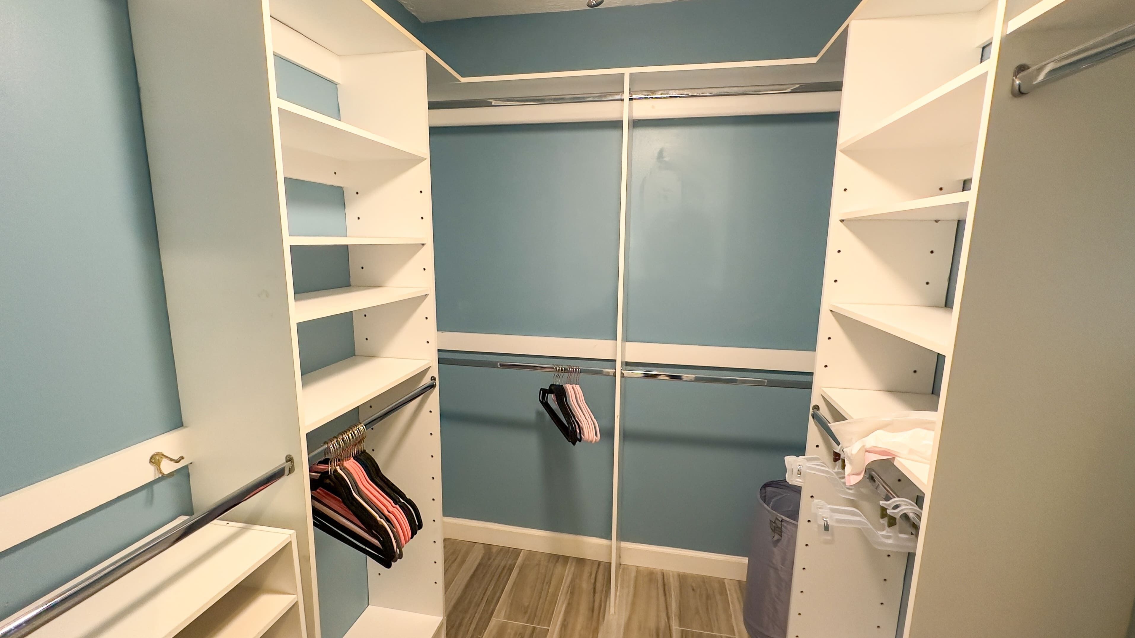 A walk-in closet with multiple shelves and hanging space, featuring a blue wall and wooden flooring.