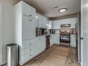Una cocina moderna con armarios blancos, electrodomésticos de acero inoxidable y piso de madera.