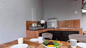 Una cucina compatta con una macchina da caffè, un bollitore e un lavandino. Un tavolo con una ciotola di frutta e una tazza è allestito per mangiare.