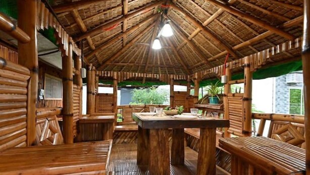 Un interno rustico in legno con tetto di paglia, panche di legno e un tavolo centrale con sedie.
