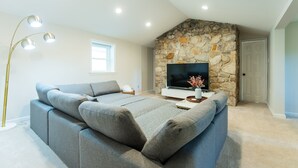 Een moderne woonkamer met een stenen openhaard, een grote grijze modulaire bank, een flatscreen-televisie en inbouwspots.