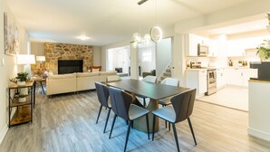 Een moderne open woon- en eetruimte met een stenen open haard, een bank, een eettafel met stoelen, en een keuken op de achtergrond.