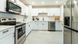Een moderne keuken met witte kastjes, roestvrijstalen apparatuur en een betegelde spatwand.