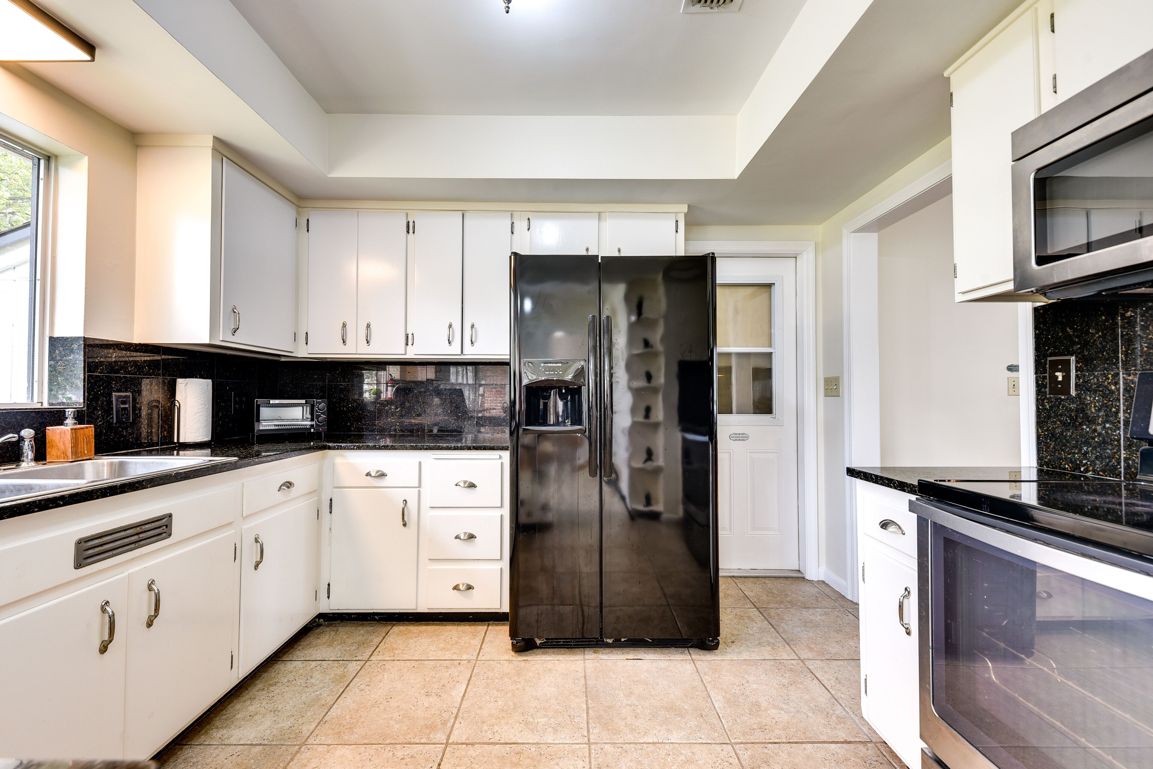 Una cocina moderna con armarios blancos, un refrigerador de acero inoxidable y una encimera negra.