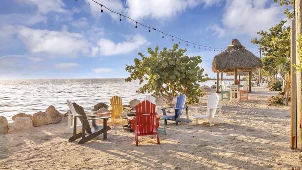 Un décor de plage avec des chaises Adirondack aux couleurs vives, une structure à toit de chaume et une guirlande de lumières.