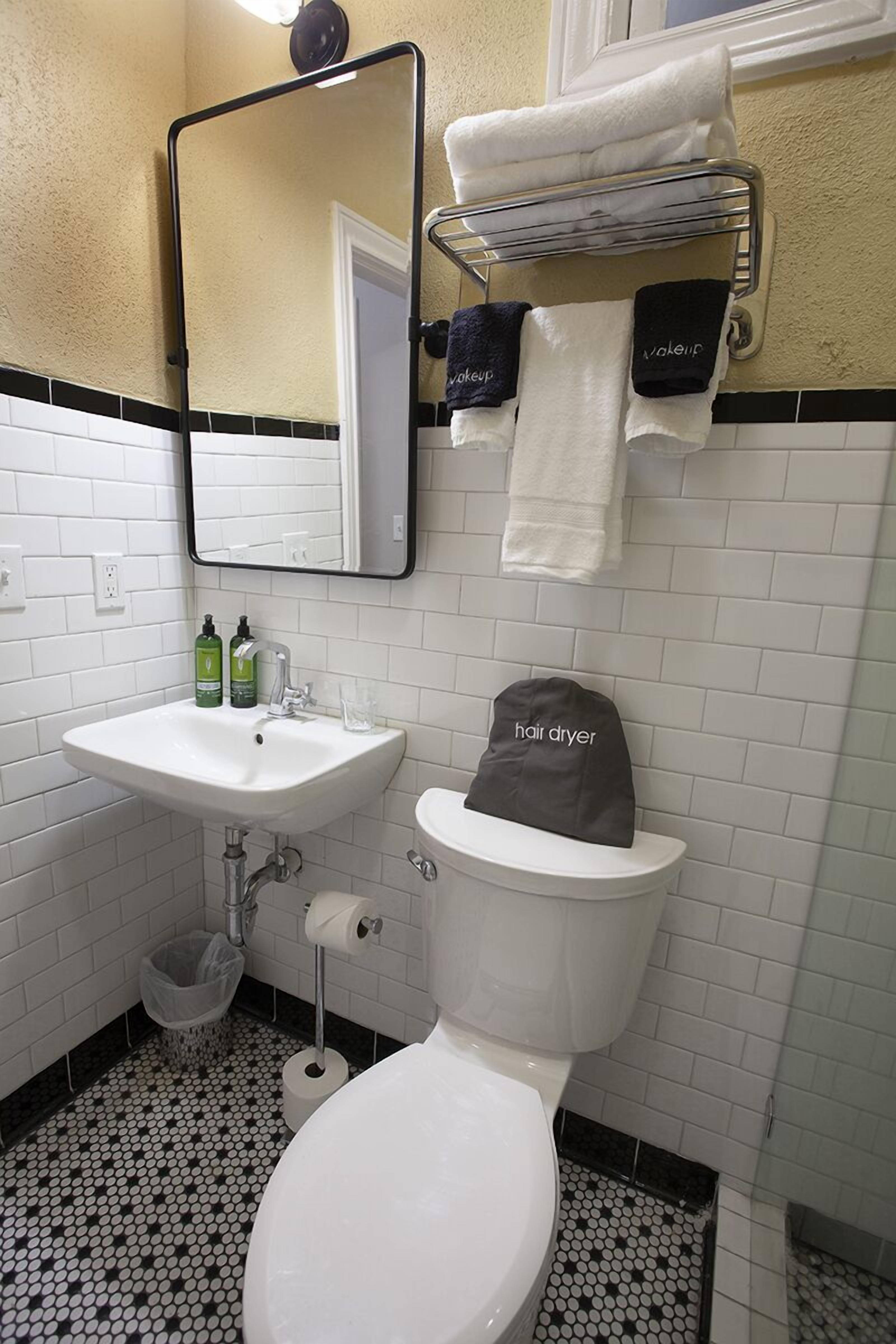 A bathroom with a white sink, mirror, toilet, and a hair dryer on the toilet.