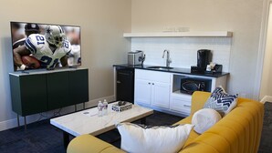 Un salon moderne avec un canapé jaune, une table basse, un téléviseur et un coin cuisine équipé d’un évier et d’appareils électroménagers.