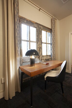 A room with a wooden desk, a black chair, a lamp, and a window with curtains.