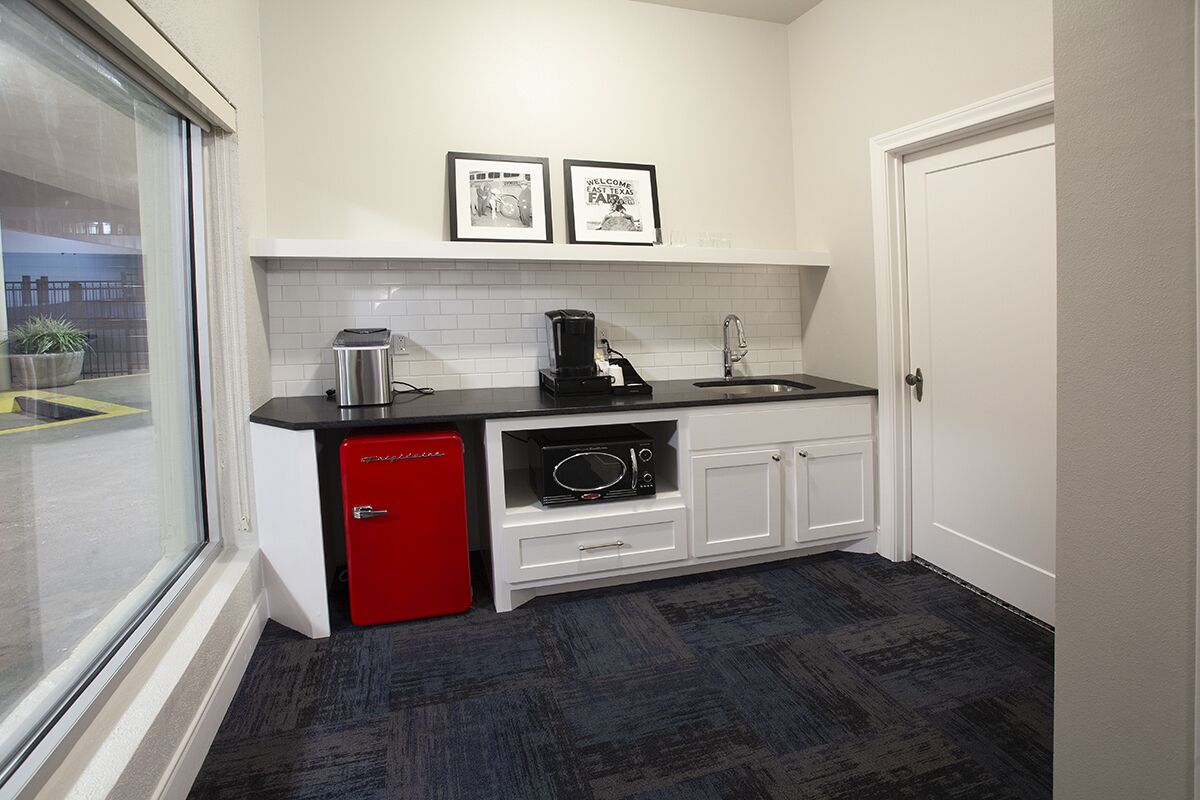 A compact kitchen with a red refrigerator, a coffee maker, and a microwave. There are two framed pictures on the wall and a window with a view of the outside.