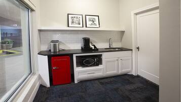 A compact kitchen with a red refrigerator, a coffee maker, and a microwave. There are two framed pictures on the wall and a window with a view of the outside.